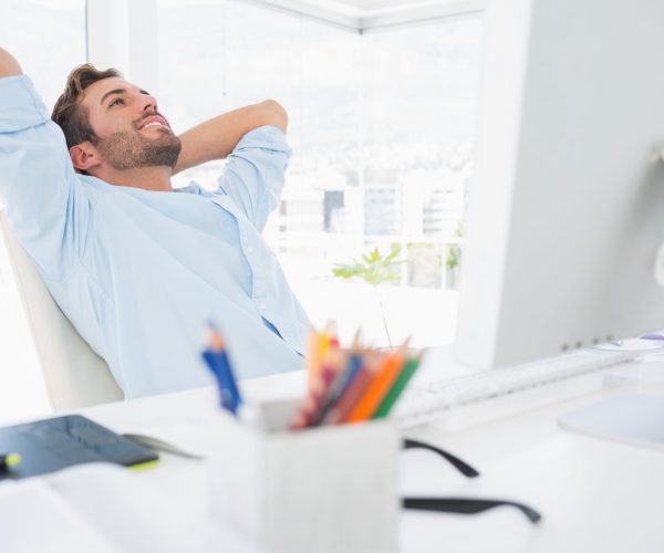 Relaxed casual young man resting with hands behind head in a bright office